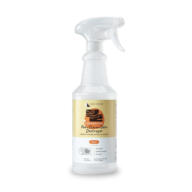 The kin+kind Pet Pee + Stain + Odor Remover Spray for Hardwood Floors comes in a white spray bottle with an orange and black label featuring a dogs head. It has a trigger nozzle and uses plant-based technology with naturally derived ingredients for superior odor elimination with a citrus scent.