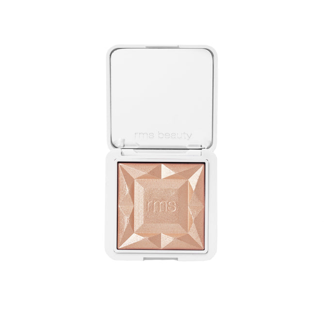 The RMS Beauty ReDimension Hydra Dew Luminizer is a square, peach-toned luminizer in a white compact marked with rms beauty inside the lid. Viewed from above, the gel-to-powder formula has a faceted, gem-like surface.