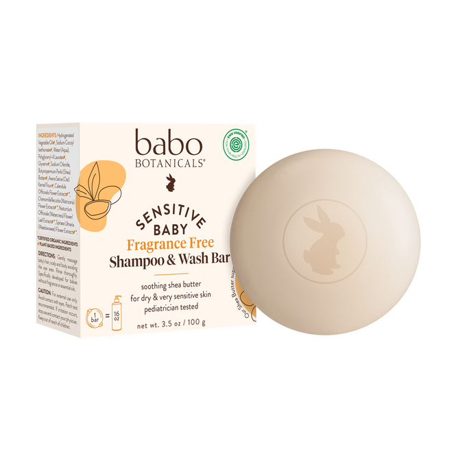 A round, beige Sensitive Baby Shampoo & Wash Bar by Babo Botanicals for sensitive skin sits beside its eco-friendly box, labeled fragrance free with a rabbit logo and ingredient details.
