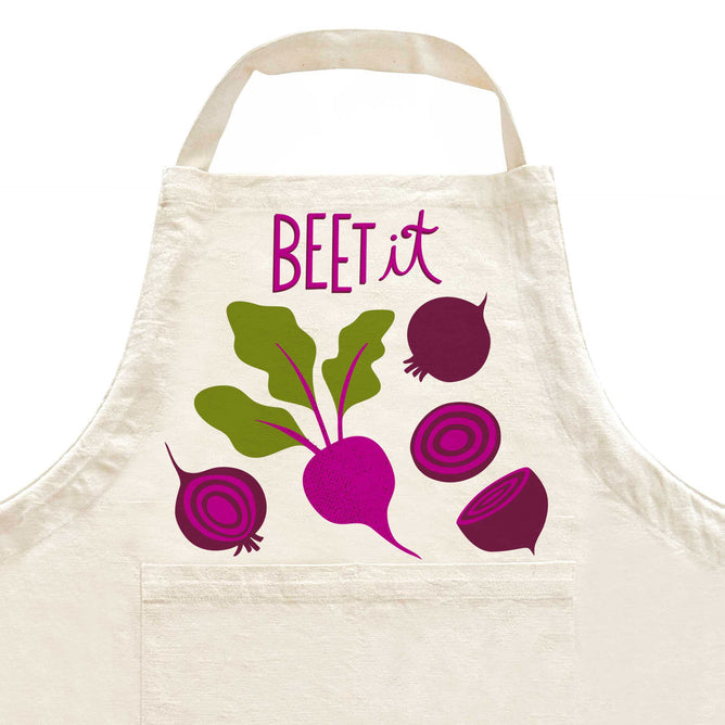 A kitchen essential, The Neighborgoods Apron features a playful beet print with slices and leaves plus “BEET it” in purple and pink letters.