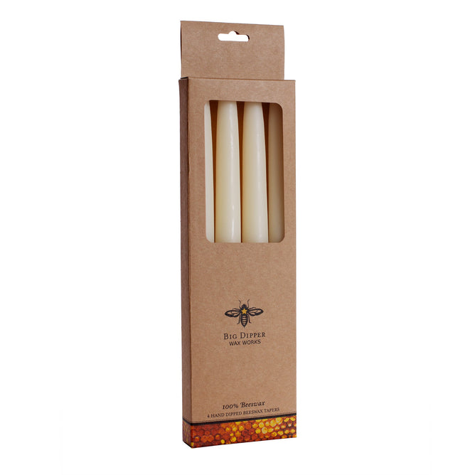A brown box with a window displays four cream-colored beeswax tapers. Labeled Big Dipper Wax Works and Hand Dipped Tapers 4 pk, the packaging highlights pure, toxin-free candles made from 100% beeswax with a bee logo.