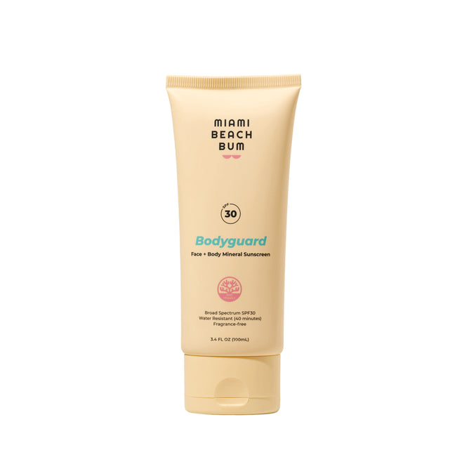 A beige tube of Miami Beach Bum Bodyguard SPF30 Face + Body Mineral Sunscreen stands upright on a white background, displaying its branding and details. This mineral sunscreen provides fragrance-free UVA/UVB protection.