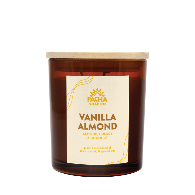 The Signature Candle - Vanilla Almond by Pacha Soap Co. features almond, cherry, and coconut scents in a brown glass jar with a wooden lid. Made from a plant-based soy, coconut & apricot wax blend, it delivers a clean, cozy burn.