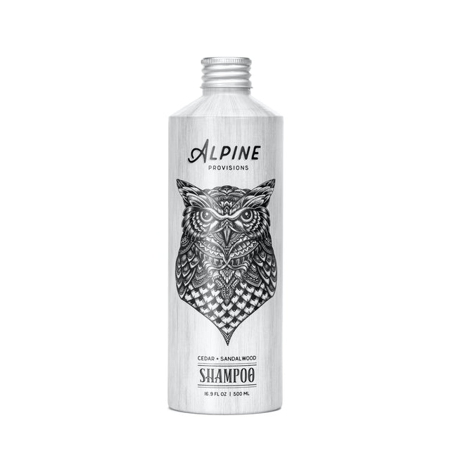 A silver Alpine Provisions Shampoo bottle, featuring a detailed black owl illustration and labeled “Cedar + Sandalwood,” 16.9 fl oz (500 mL), highlights natural hair care with essential oil aromatherapy on a white background.
