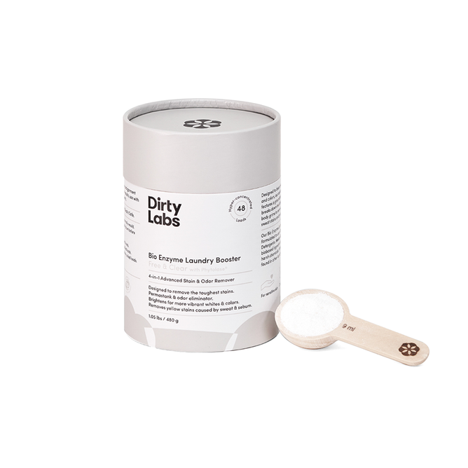 A cylindrical Dirty Labs Bio Enzyme Laundry Booster is next to a wooden scoop full of powder. The minimalist design emphasizes enzyme technology with text and icons showcasing its environmental benefits and effectiveness against biological stains.
