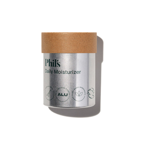A silver cylindrical container with a brown lid, labeled Phils Daily Moisturizer - RePhil. Eco-friendly icons and text appear on the bottom. Enriched with prebiotics, it casts a shadow against a white background.