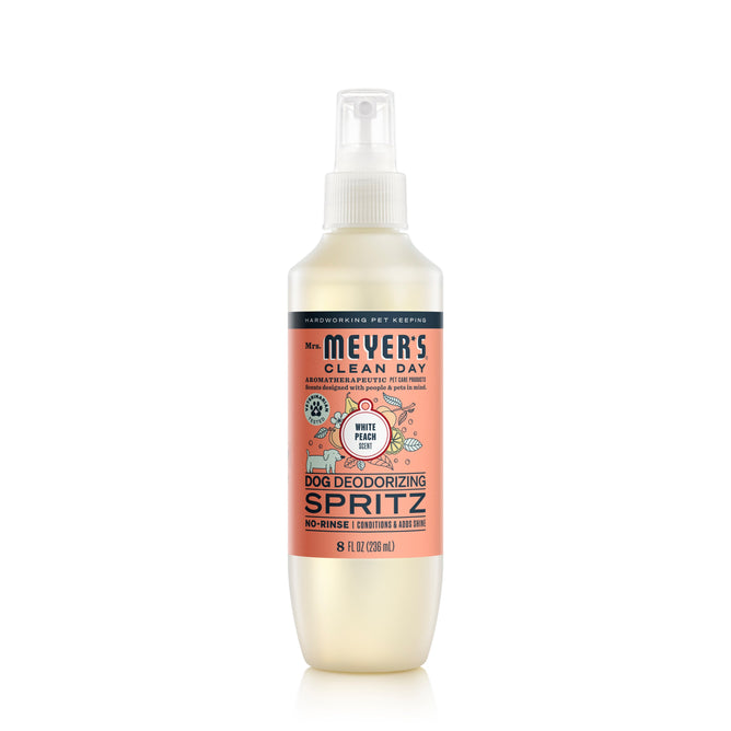 Mrs. Meyers Dog No-Rinse Shampoo in a sleek white bottle with pink and silver labels enhances your dogs coat with a white peach scent and shine, featuring stylish dog care graphics.