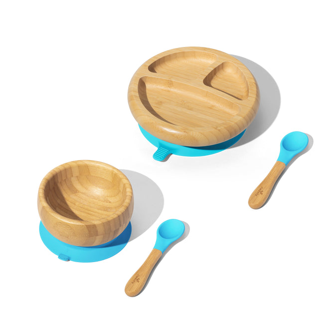 The Essential Bamboo Baby and Toddler Dish Set by Grove Collaborative features a wooden bowl and sectioned plate with blue silicone bases, displayed alongside two wooden-handled baby spoons with blue silicone tips on a white background.