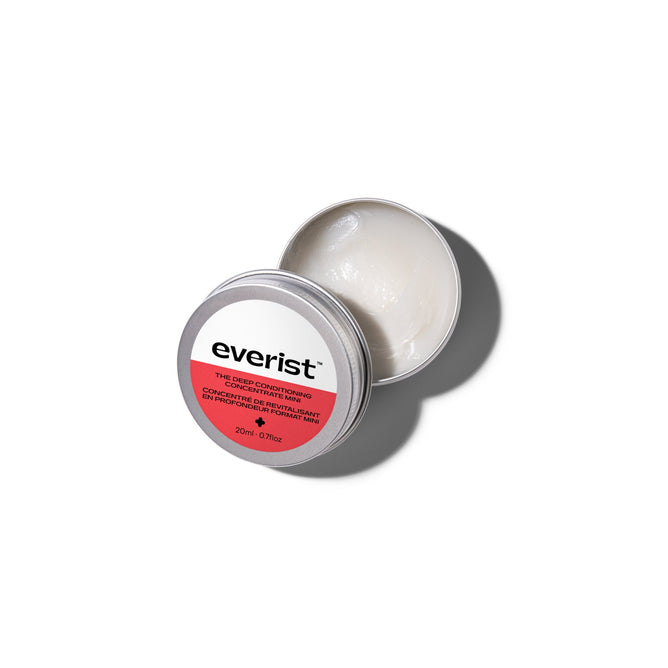 An open round metal tin of Everist The Deep Conditioning Concentrate Travel Mini reveals a creamy white formula, while its pink and white label conveys innovative haircare inspired by skincare.