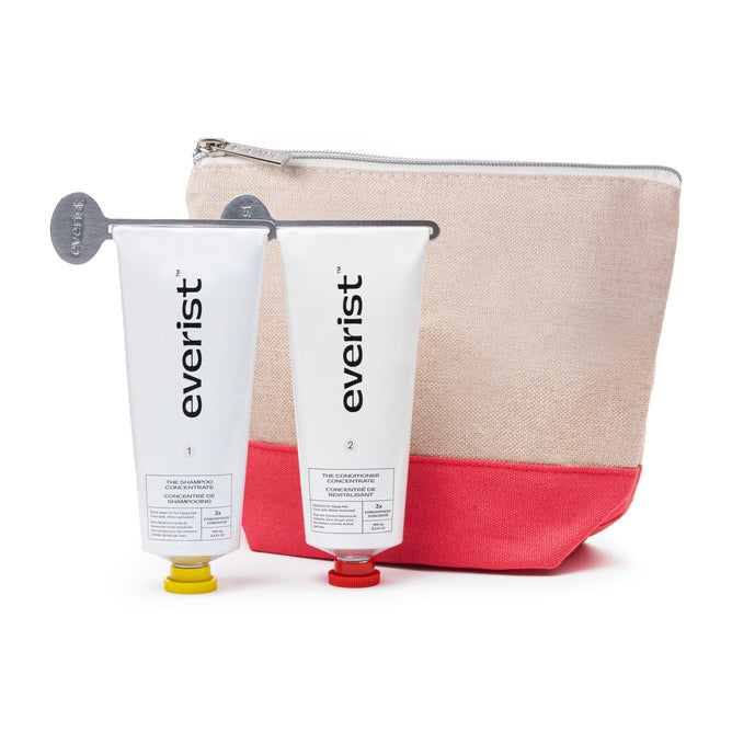 Everist’s The Haircare Meets Skincare Set features two tubes—Shampoo Concentrate and Conditioner Concentrate—with metal keys, displayed in front of a beige and pink zippered pouch for deep hydration.