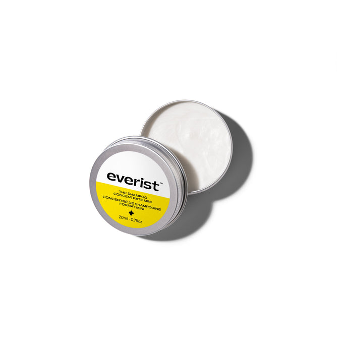 A round, silver tin container of Everist’s The Shampoo Concentrate Travel Mini sits open on a white background, revealing a creamy, plant-based formula. The lid features the Everist label in yellow and white with product information.