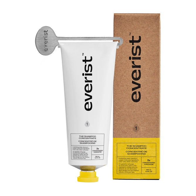 A white metal tube labeled Everist The Shampoo Concentrate with a metal key sits beside a brown box with yellow and white labels, showcasing Everist’s plant-based haircare against a white background.