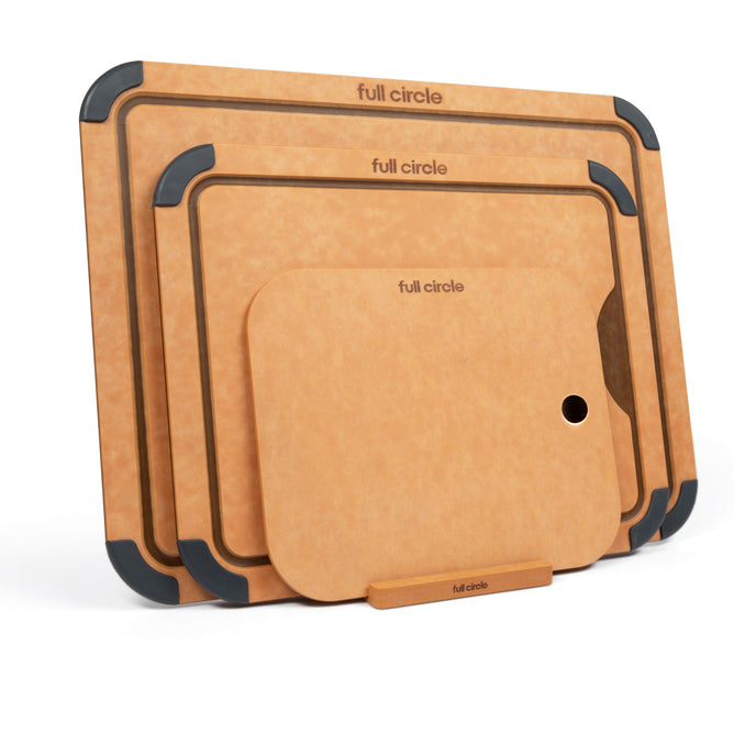 The Cutting Board Set with Holder by Full Circle includes three brown, dishwasher-safe, antibacterial boards of varying sizes in a stand. Each board has black-edged accents, and the largest has a corner hole.