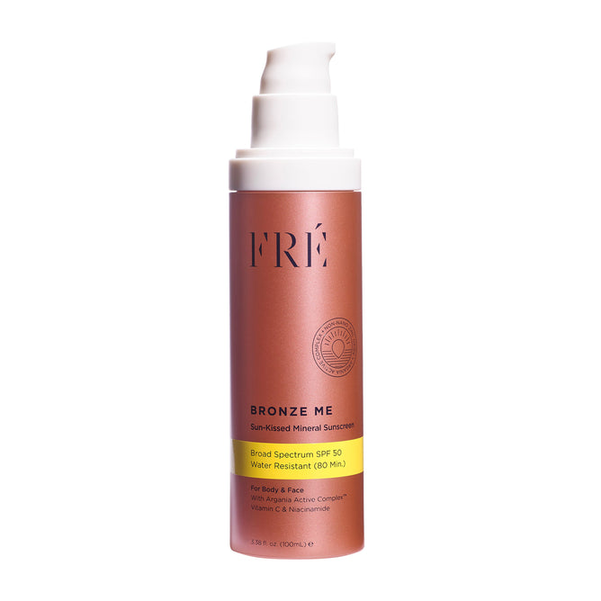 A bronze pump bottle of FRÉ Skincare BRONZE ME Sun-Kissed Mineral Sunscreen SPF 50, water-resistant for 80 minutes with vitamin C, niacinamide, and argan antioxidants for a shimmery finish on body and face, on a white background.