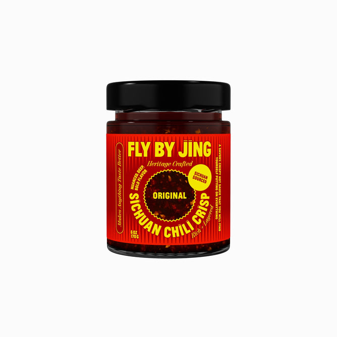 A jar of Fly By Jing Original Sichuan Chili Crisp hot sauce with a red and yellow label, black lid, and text emphasizing its all-natural Sichuan-sourced ingredients sits on a white background.