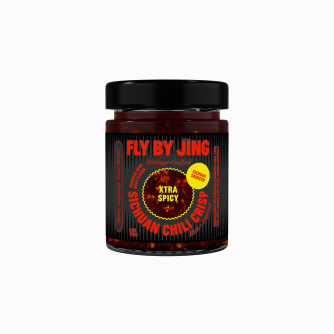 A glass jar of Fly By Jing Xtra Spicy Sichuan Chili Crisp features bold red and yellow text on a black label. Filled with hot Chinese chilis in dark red chili oil, it has a black lid and delivers extra spicy flavor.