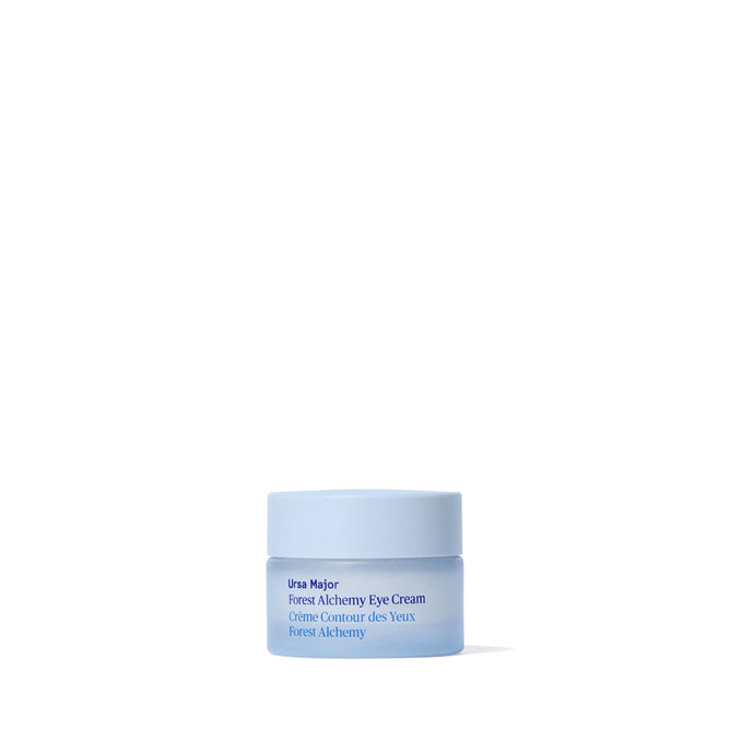 A small, light blue jar of Ursa Major Forest Alchemy Eye Cream—formulated to reduce dark circles and fine lines—rests on a plain white background. The label shows both English and French text.