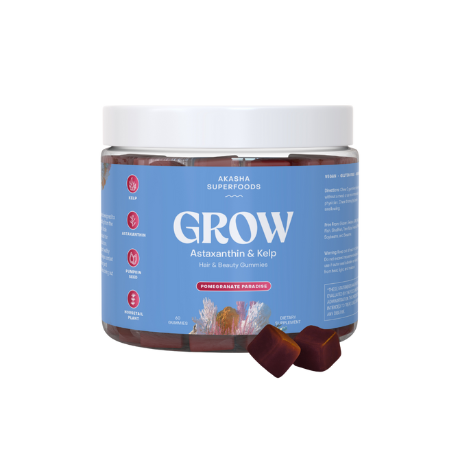 A clear plastic jar labeled GROW Hair & Beauty Gummies by Akasha Superfoods contains red gummies, with several in front. The light blue label with white and pink text highlights hair growth support.