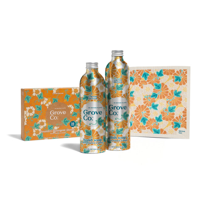 Two bottles and a box of Grove Co. Scent Essentials - Fall Collection cleaning products with orange and teal floral packaging are displayed beside a matching cloth, all featuring limited edition scents, on a white background.