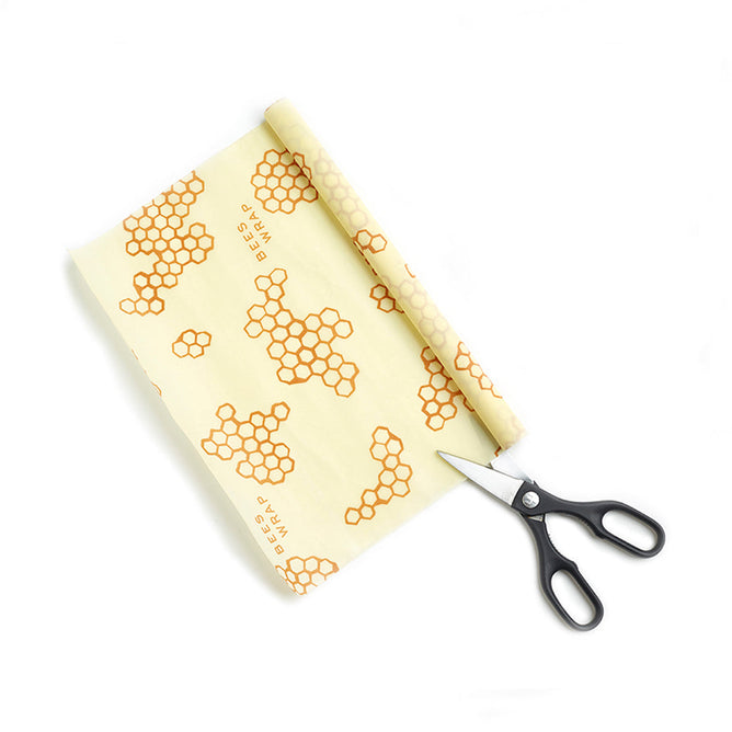 Bees Wrap XXL Roll Wrap, featuring an orange honeycomb pattern, is partially unrolled beside black-handled scissors on a white background, providing a reusable and plastic-free way to store food.