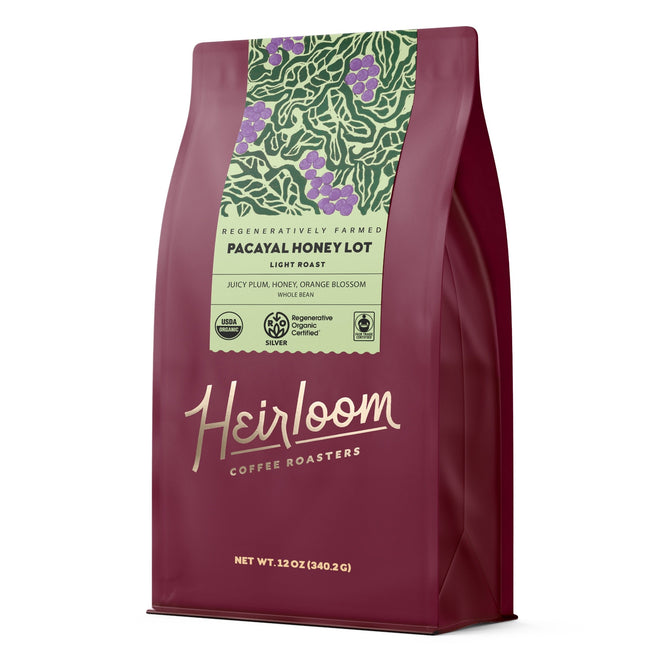 A maroon bag of Heirloom Coffee Roasters Pacayal Honey Lot ROC Whole Bean Coffee, a honey-processed single origin featuring green leaf and fruit art. Showcases regenerative farming and flavors of juicy plum, honey, and orange blossom.