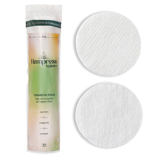 A package of Hempress Hygienics Hemp Cosmetic Rounds stands upright beside two round pads—one textured, one smooth. The packaging promotes hypoallergenic, pesticide-free hemp fiber, organic cotton, and eco-friendly qualities.