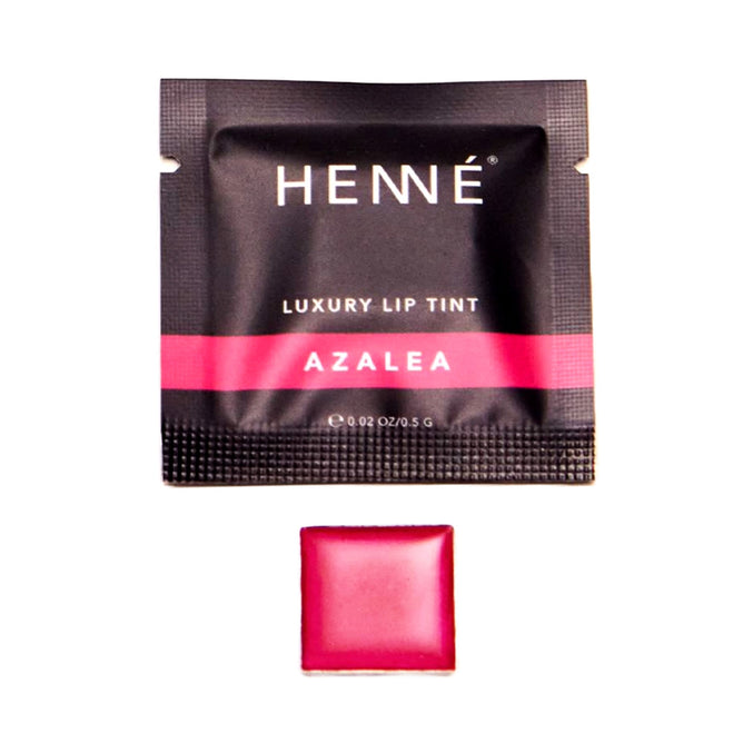 A black sachet labeled Henné Organics Luxury Lip Tint - Sample with a pink stripe, pictured above a square pan holding vibrant, hydrating lip color in a striking pink shade.