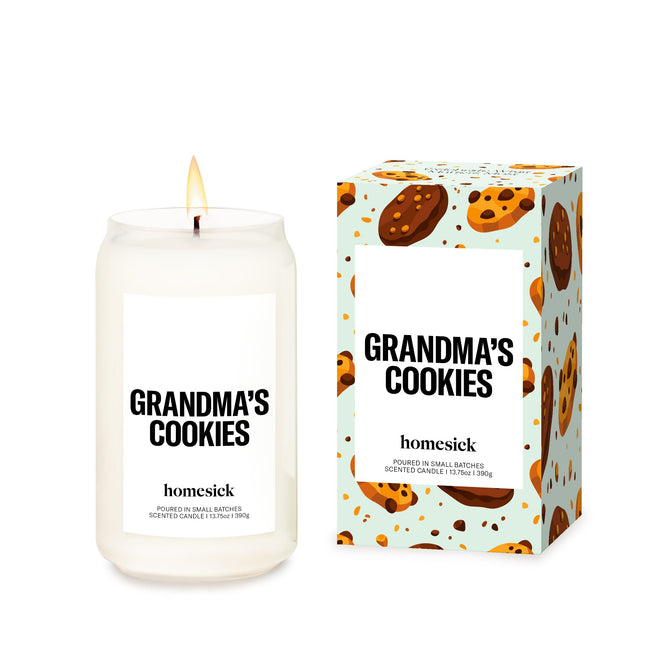 A lit Grandmas Cookies Candle by Homesick sits next to its packaging adorned with cookie illustrations. Made from natural soy wax in a reusable glass jar, both the box and candle highlight the Homesick brands commitment to cruelty-free products.