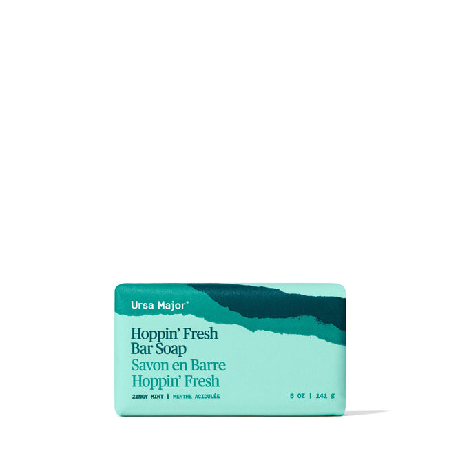A turquoise bar of Ursa Major Morning Mojo Bar Soap in its packaging, with white and dark teal text and a wavy dark teal design on top. Made with natural products, this zesty mint exfoliating soap comes in a 5 oz size.
