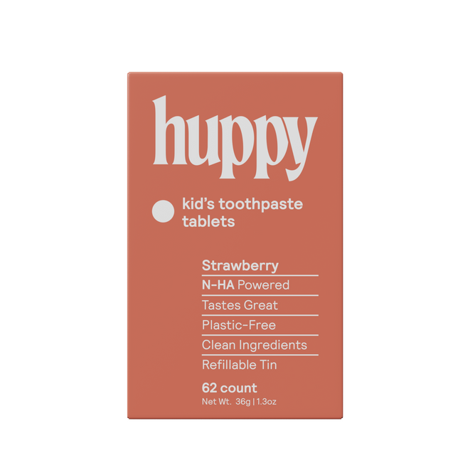 A rectangular orange box labeled Huppy Kids n-HA Toothpaste Tablets with Tin, featuring strawberry flavor, cavity-fighting nano-hydroxyapatite, clean ingredients, a plastic-free refillable tin, and 62 tasty tablets.