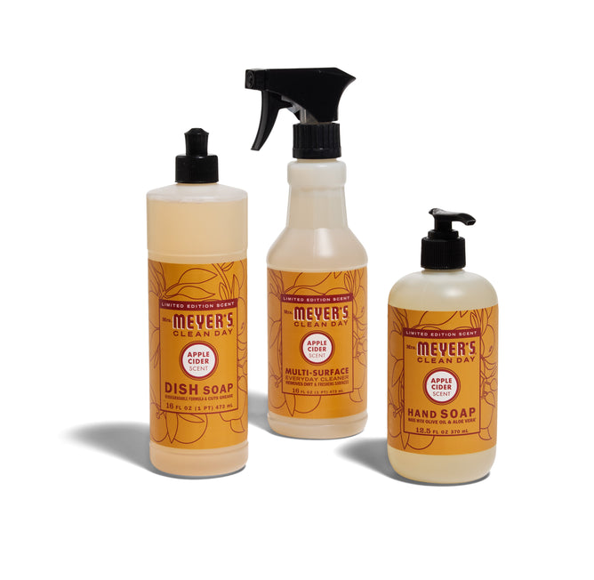 The Mrs. Meyers Happy Harvest Essentials Set - Apple Cider includes dish soap, multi-surface cleaner, and hand soap in apple cider scent with orange labels.