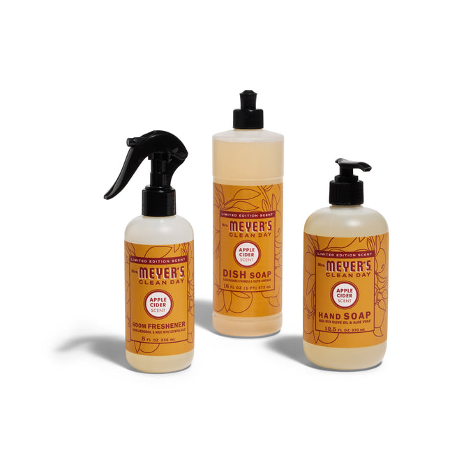 The Mrs. Meyers Harvest Home Helpers Set in Apple Cider includes a room spray, dish soap, and hand soap, each with coordinated orange and yellow labels shown together on a white background.