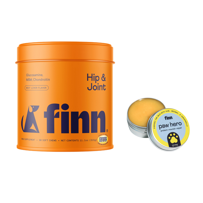 An orange container labeled Finn Hip & Joint Supplement for Dogs + free gift sits beside an open tin labeled Finn Paw Hero. The tin holds a balm. Both Finn products are designed for pet care—one supports joints, and the other promotes paw health.