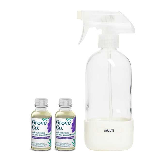 Two small bottles labeled Multi-Purpose Cleaner Starter Set from Grove Collaborative stand beside a transparent glass spray bottle with a white nozzle and base labeled MULTI, all featuring elegant purple lavender illustrations.