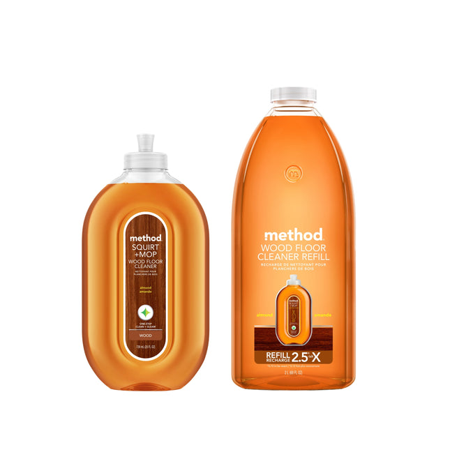 Two orange bottles of methods Squirt Mop Wood Floor Cleaner Starter Set in Almond are shown; the smaller has a squirt mop cap, while the larger is a wood floor cleaner refill. Both have clean, modern labels.
