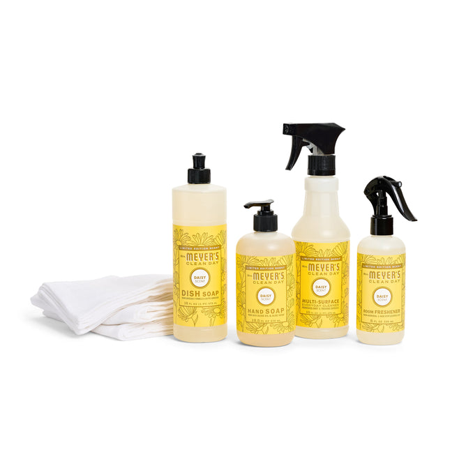 Mrs. Meyers Sinkside Spring Cleaning Set, featuring eco-friendly dish soap in yellow containers, includes hand soap, multi-surface cleaner, and room freshener, displayed with folded white organic cotton towels on a white background.