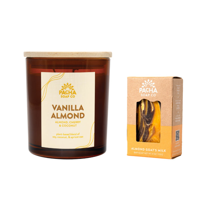A Pacha Soap Co. brown glass Signature Candle sits beside a free bar of Almond Goats Milk soap, visible through the box window—part of the Buy a Signature Candle, Get a Bar Soap Free offer.