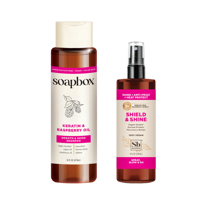 Against a white backdrop are two hair care products: Soapboxs Vegan Keratin & Raspberry Seed Oil Smoothing Shampoo and SB Shield & Shine spray with bamboo and marula butter for shine, anti-frizz, and heat protection. Both boast vegan labels.
