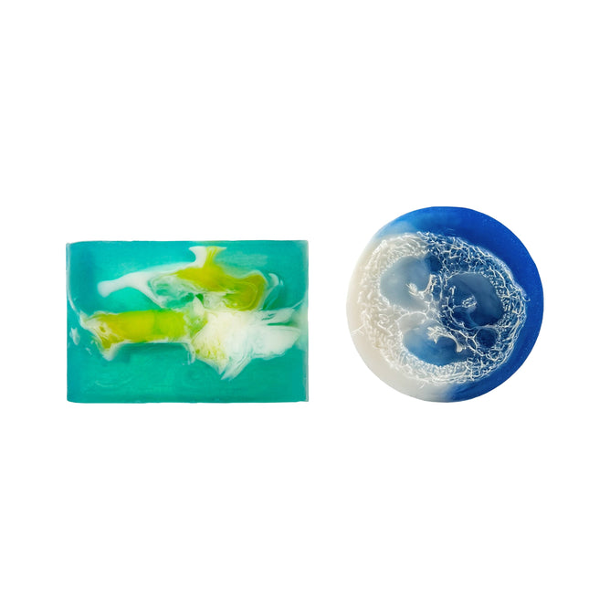 The Grove Collaborative Hawaiian Paradise Soap Bar features a rectangular turquoise design with white and yellow swirls, displayed beside a round Tropical Plumeria Loofah soap. Limited time offer: includes free gift. Arranged on a white background.