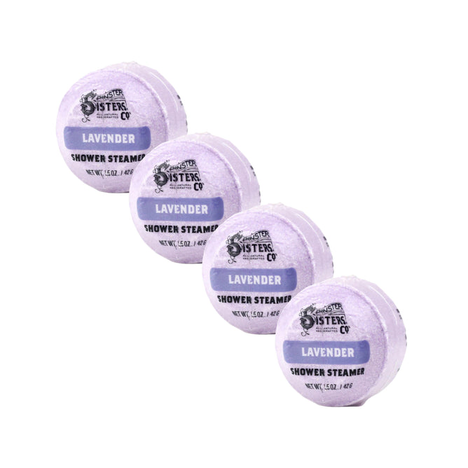 Four round Lavender Shower Steamers from Spinster Sisters Co., infused with essential oils, are arranged diagonally on a white background. Each steamer is labeled with “Spinster Sisters Co.” and “Lavender Shower Steamer.”.
