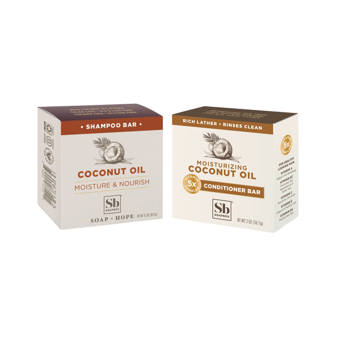 Soapbox Moisturizing Coconut Oil Haircare Set includes a shampoo bar and conditioner bar in brown and beige boxes with coconut illustrations, offering nourishing, eco-friendly hair care on a white background.