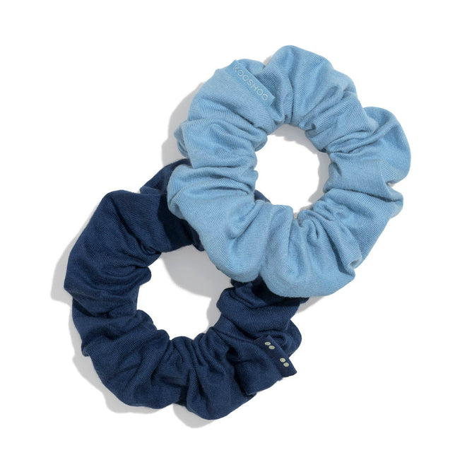 Two KOOSHOO Scrunchies, in light and dark blue, overlap on a white background. These zero waste hair accessories combine style and sustainability for everyday wear.