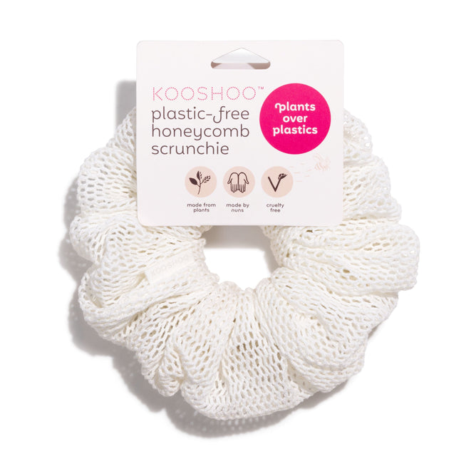 A KOOSHOO Honeycomb Scrunchie, white and textured with an oversized mesh design, is shown in packaging labeled plastic-free and handmade from organic cotton, highlighting its honeycomb weave and cruelty-free origins.
