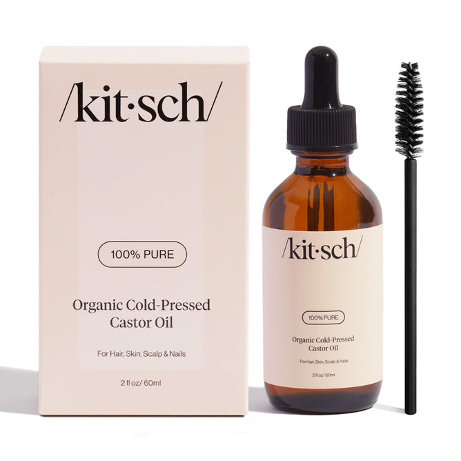Kitschs 100% Pure Castor Oil bottle is displayed with its packaging and a black applicator brush. Featuring a dropper top and minimalist label, the omega-rich formula promotes healthier scalp care while nourishing hair, skin, and nails.