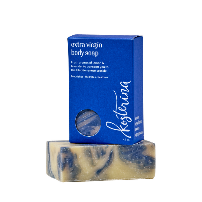 A bar of Kosterina Extra Virgin Body Soap with blue and cream swirls peeks from a blue box with a circular window, capturing the spirit of the Mediterranean seaside in every use.