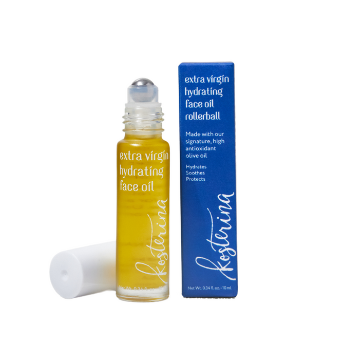 A clear glass bottle of Kosterina Extra Virgin Hydrating Face Oil - Rollerball stands beside its blue box, offering a dewy glow and lasting hydration for your skin.