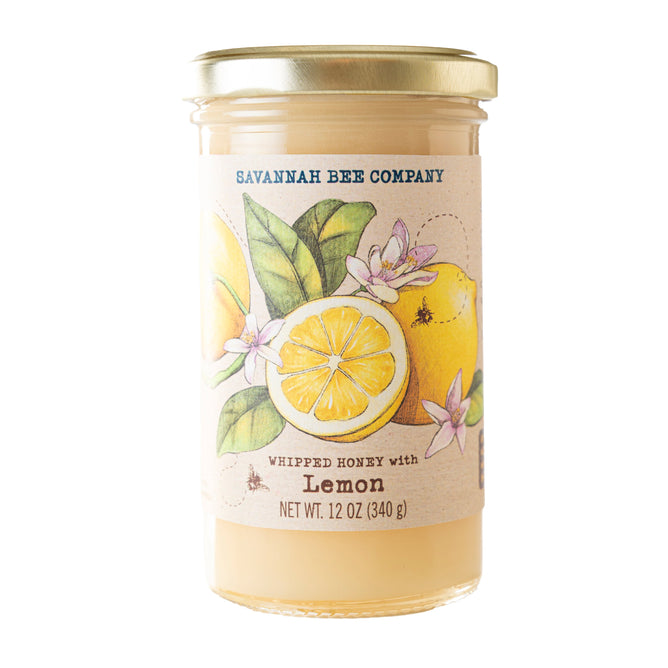 A 12 oz (340 g) glass jar of Savannah Bee Company Whipped Honey with Lemon, made with organic lemon oil and topped with a gold lid; the label shows lemons, leaves, and blossoms.