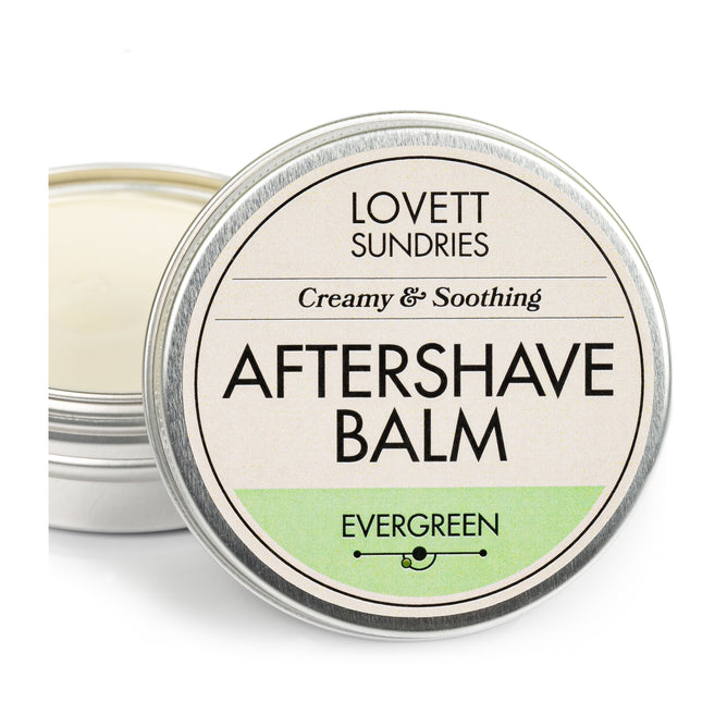A round metal tin of Lovett Sundries Aftershave Balm features a Creamy & Soothing and Evergreen label with the lid slightly ajar, exposing the creamy balm ideal for soothing skin and preventing razor burn.
