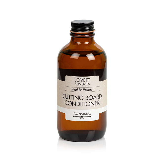 A brown glass bottle of Lovett Sundries Cutting Board Conditioner with a black screw cap stands on a white background. The label highlights Seal & Protect and infused coconut oil for all-natural wood protection.