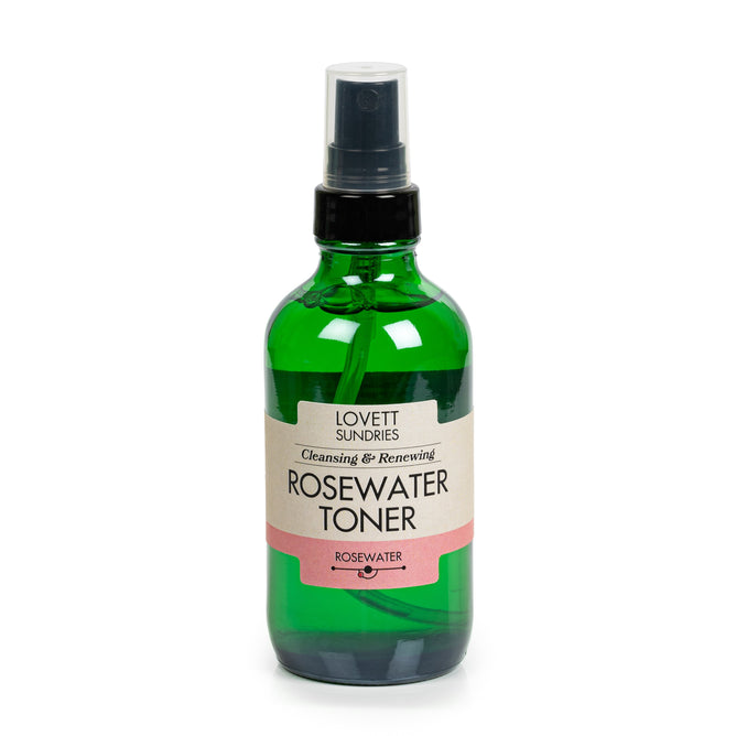 A green spray bottle of Lovett Sundries Rosewater Toner, featuring a black spray top and beige-pink label, is displayed against a white background.